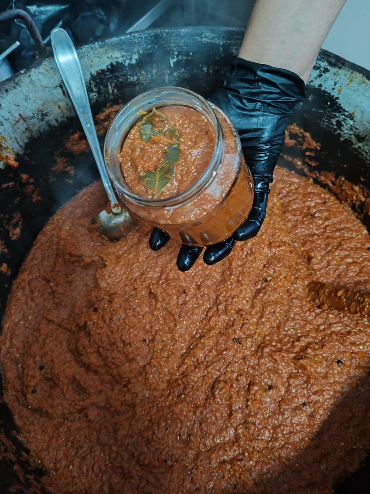 Borcan de zacuscă ținut deasupra ceaunului plin, cu o foaie de dafin deasupra
